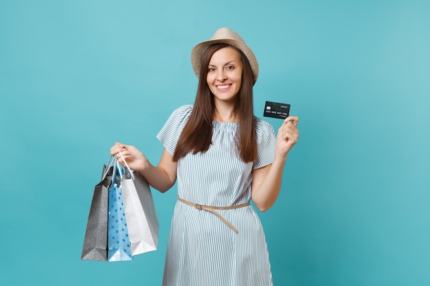 Retrato de hermosa mujer caucásica en vestido de verano, sombrero de paja con bolsas de paquetes con compras después de ir de compras, tarjeta de crédito bancaria aislada sobre fondo azul pastel. Copie el espacio para publicidad.