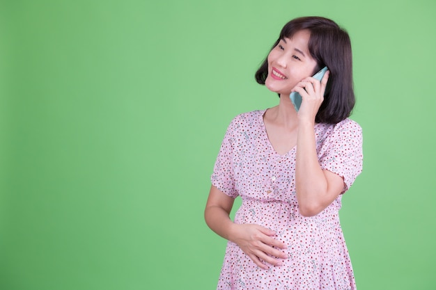 Retrato de hermosa mujer embarazada asiática con pelo corto contra chroma key o pared verde