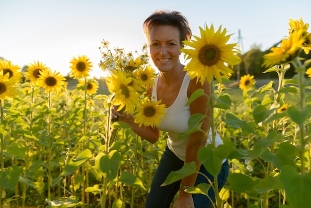 Retrato de hermosa mujer escandinava madura en el campo de girasoles florecientes al aire libre