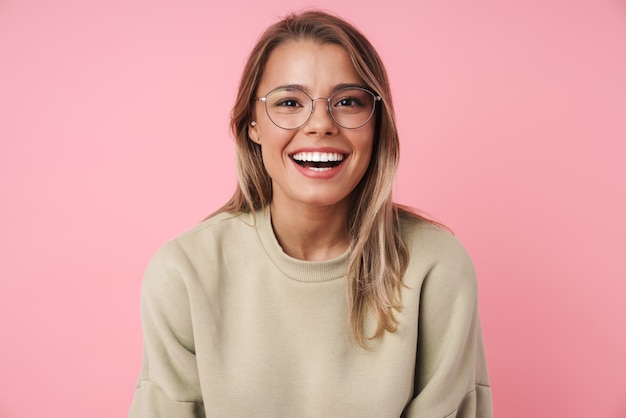 Retrato de hermosa mujer feliz en anteojos sonriendo aislado en rosa