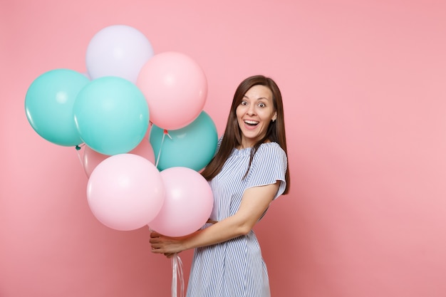 Retrato de hermosa mujer feliz joven alegre con vestido azul sosteniendo globos de aire coloridos aislados sobre fondo rosa de tendencia brillante. Fiesta de cumpleaños, concepto de emociones sinceras de personas.