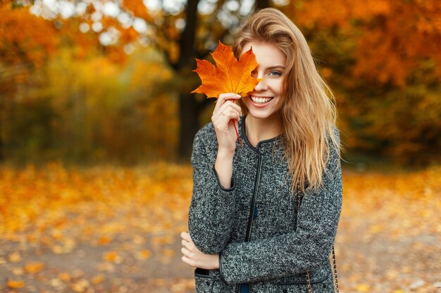 Retrato de una hermosa mujer feliz con una sonrisa con una hoja amarilla otoñal en el parque