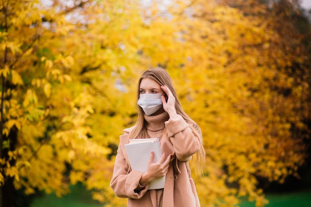 Retrato de una hermosa mujer joven adulta en el fondo del otoño en el parque en mascarilla médica