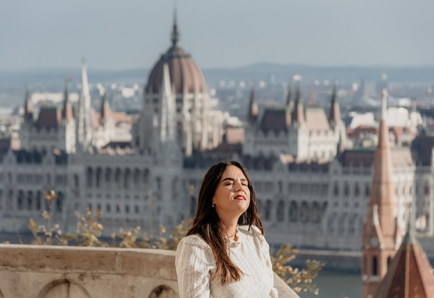 Foto retrato de una hermosa mujer joven en un balcón con vistas al parlamento húngaro en budapest, hungría