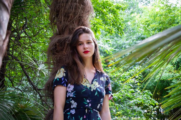 Foto retrato de una hermosa mujer joven contra el tronco de un árbol en el bosque