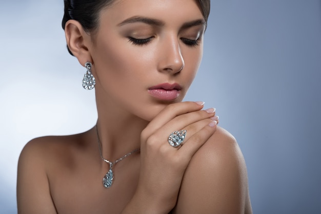 Foto retrato de una hermosa mujer joven elegante con aretes de diamantes anillo y collar posando con los ojos cerrados