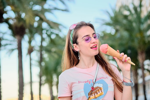 Retrato de hermosa mujer joven feliz en gafas de sol de color rosa comiendo helado de color rosa.