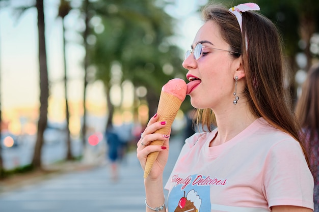 Retrato de hermosa mujer joven feliz en gafas de sol de color rosa comiendo helado de color rosa.