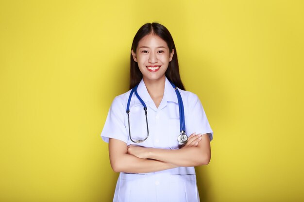 Retrato de una hermosa mujer joven con un fondo amarillo mujer asiática que lleva un uniforme de médico hace una expresión sonriente una mujer joven que lleva un estetoscopio médico tiene una expresión amistosa