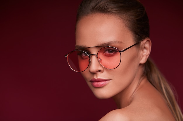 Retrato de hermosa mujer joven con gafas de sol rojos. Modelo de moda sensual