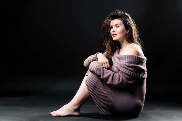 Retrato de hermosa mujer joven con hermoso cabello y maquillaje natural sentado en el piso en vestido de punto