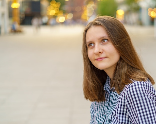 Retrato de hermosa mujer joven con largo cabello rubio mirando a otro lado contra la vista de la ciudad