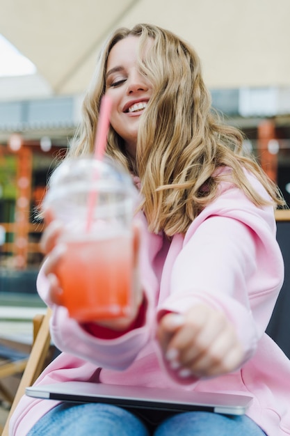 Retrato de una hermosa mujer joven con limonada Hipster en una sudadera con capucha y jeans Street cafe