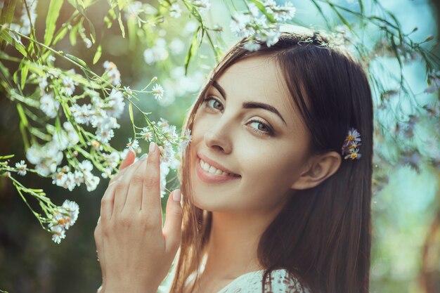 Retrato de hermosa mujer joven morena en prado de flores sonriendo y mirando a la cámara