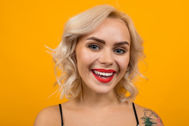 Retrato de hermosa mujer joven con pelo corto y rizado rubio y sonrisas de maquillaje brillante, retrato aislado en naranja