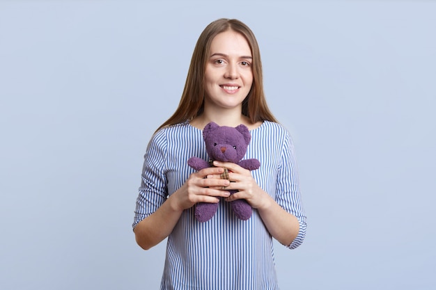 Retrato de hermosa mujer joven con el pelo largo y liso tiene oso de peluche en las manos