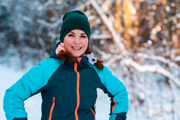 Retrato de hermosa mujer joven positiva feliz de pie en un bosque de invierno en un día frío y soleado