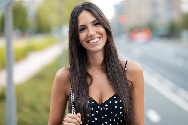 Foto retrato de hermosa mujer joven sonriendo mientras mira a la cámara de pie en la calle.