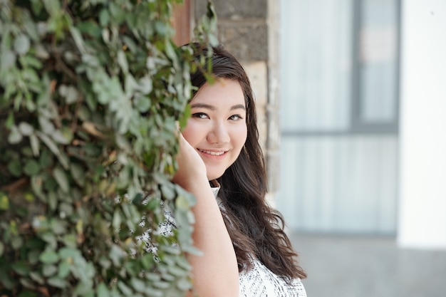 Retrato de hermosa mujer joven sonriente de pie en la pared cubierta de hiedra y sonriendo a la cámara