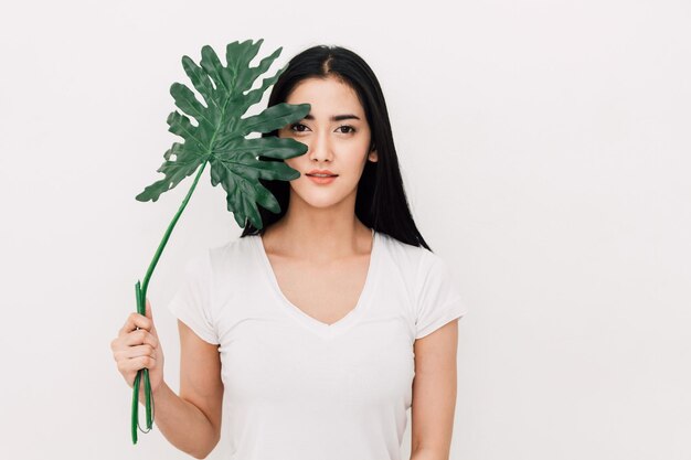 Retrato de una hermosa mujer joven sosteniendo una planta contra un fondo blanco