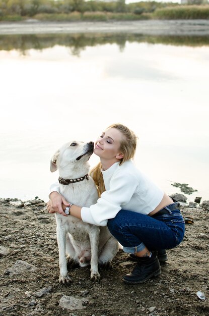 Retrato de una hermosa mujer joven con su lindo perro blanco en la naturaleza al aire libre vertical de cuerpo entero