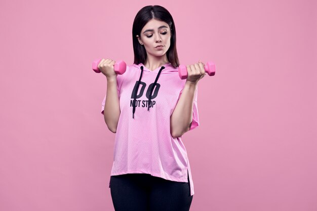 Foto retrato de una hermosa mujer latina positiva del cuerpo en una sudadera deportiva rosa con ejercicio con pesas en rosa