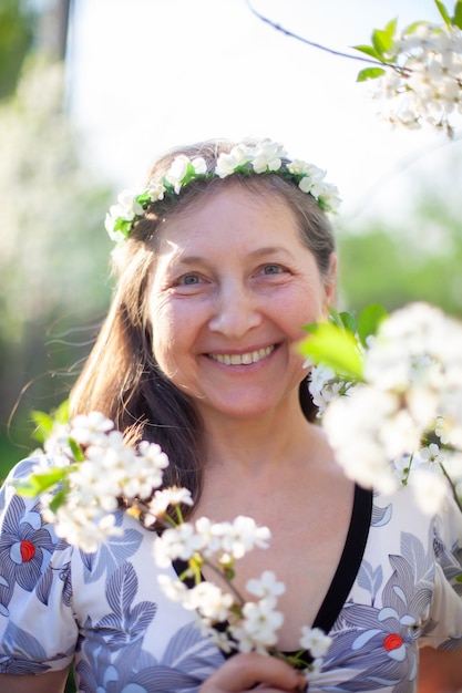 Retrato de una hermosa mujer madura con un vestido ligero contra el fondo de los jardines florecientes de primavera