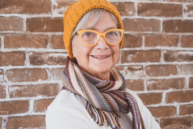 Foto retrato de hermosa mujer mayor vistiendo gorro y bufanda de invierno - fondo de pared de ladrillo