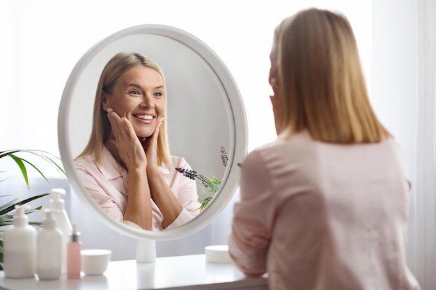 Retrato de una hermosa mujer de mediana edad mirando al espejo y tocando la cara