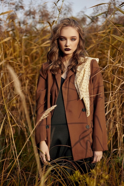 Retrato de una hermosa mujer de moda en un matorral de hierba de otoño