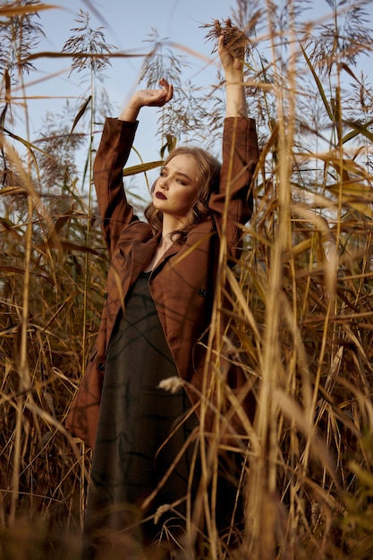 Retrato de una hermosa mujer de moda en un matorral de hierba de otoño