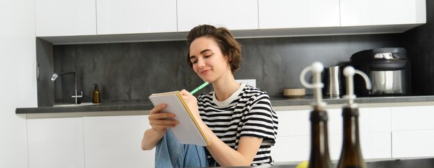Retrato de una hermosa mujer moderna cocinando con verduras sosteniendo un cuaderno escribiendo una receta