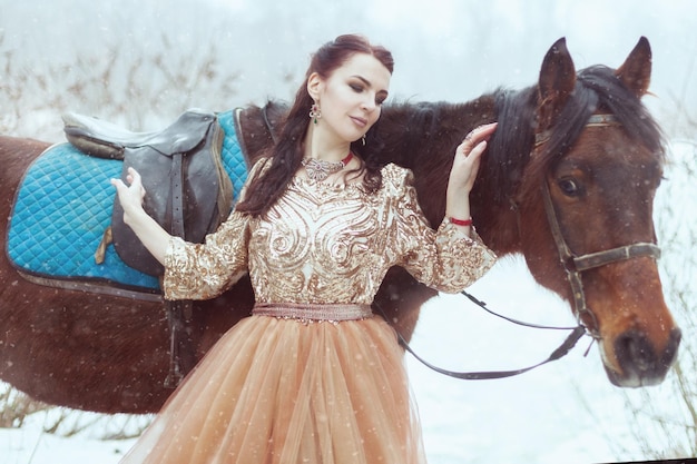 Retrato de una hermosa mujer morena cerca de un caballo en un parque de invierno