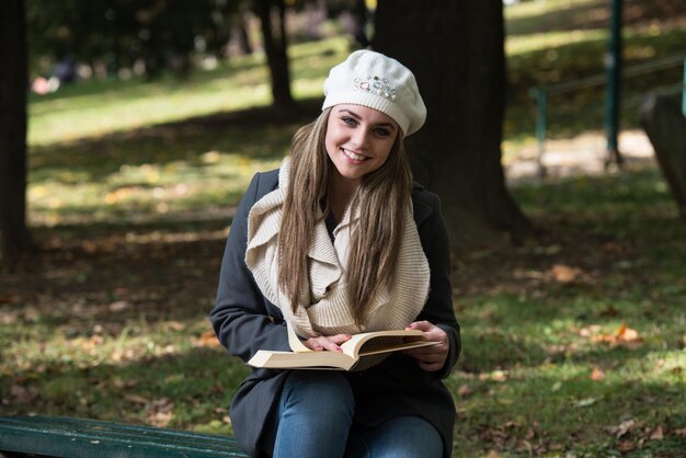 Retrato de una hermosa mujer morena leyendo un libro en el parque de otoño