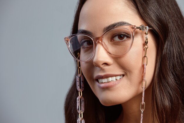 Retrato de una hermosa mujer morena en primer plano de gafas, mujer atractiva en gafas elegantes sobre un fondo gris con piel de color hermoso saludable, fondo gris, espacio de copia.