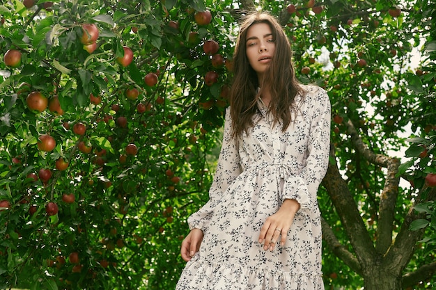 Retrato de hermosa mujer morena en vestido clásico de moda posando entre un manzano