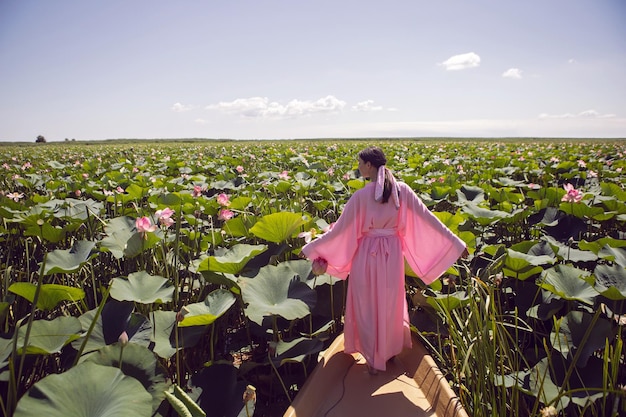 Retrato hermosa mujer morena con un vestido rosa está de pie en un barco entre lotos florecientes en un lago en Astrakhan