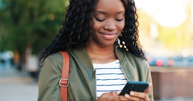 Retrato de la hermosa mujer multirracial que muestra una sonrisa encantadora y dientes sanos mientras camina con su teléfono inteligente en la calle. Concepto de personas y gadgets