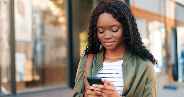 Retrato de la hermosa mujer multirracial que muestra una sonrisa encantadora y dientes sanos mientras camina con su teléfono inteligente en la calle. Concepto de personas y gadgets