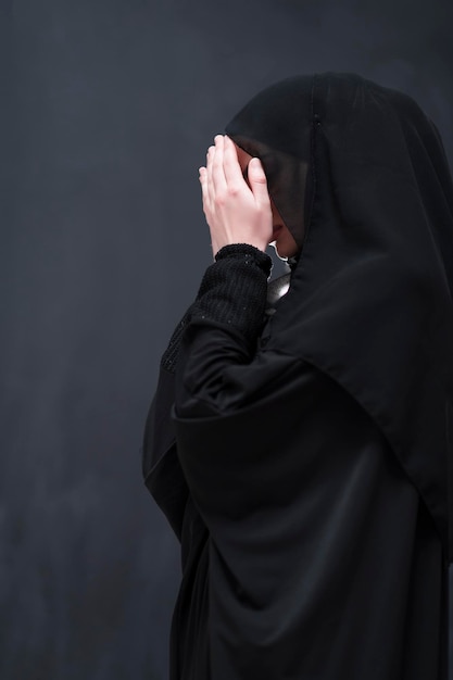 Retrato de una hermosa mujer musulmana vestida de moda con hiyab haciendo oración tradicional a Dios mantiene las manos en gesto de oración aislado en el fondo negro. foto de alta calidad