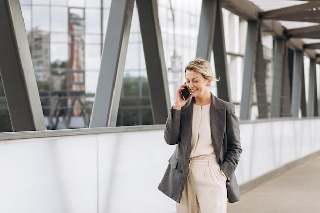 Retrato de una hermosa mujer de negocios madura con traje y chaqueta gris sonriendo y hablando por teléfono en un moderno fondo urbano y de edificios de oficinas