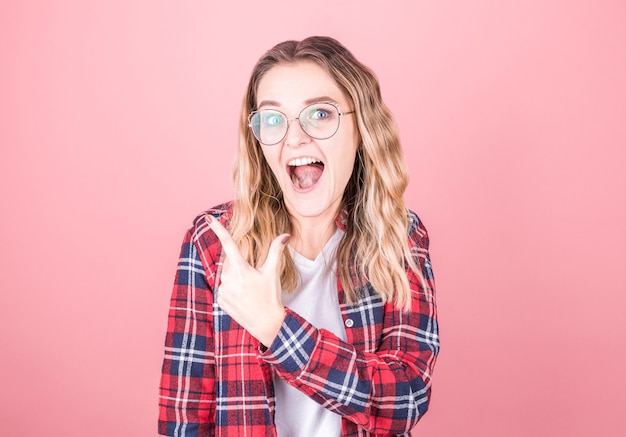 Retrato de hermosa mujer rubia apuntando con el dedo aislado sobre fondo rosa con copyspace