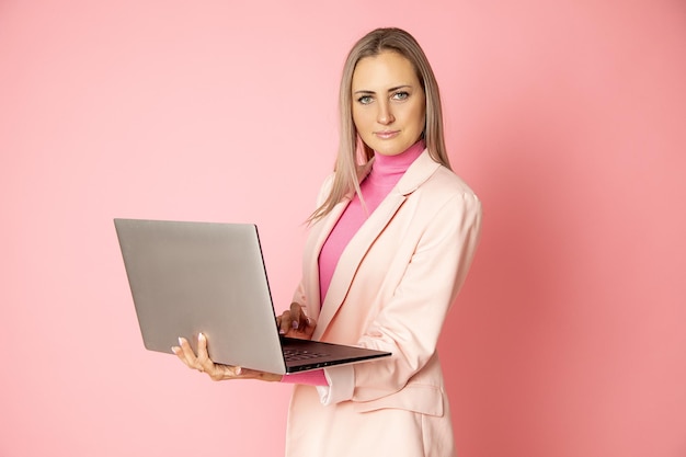 Retrato de hermosa mujer rubia blanca con portátil sobre fondo rosa en estudio, mirando seriamente a cámara, concepto de gente de negocios. Ropa de negocios