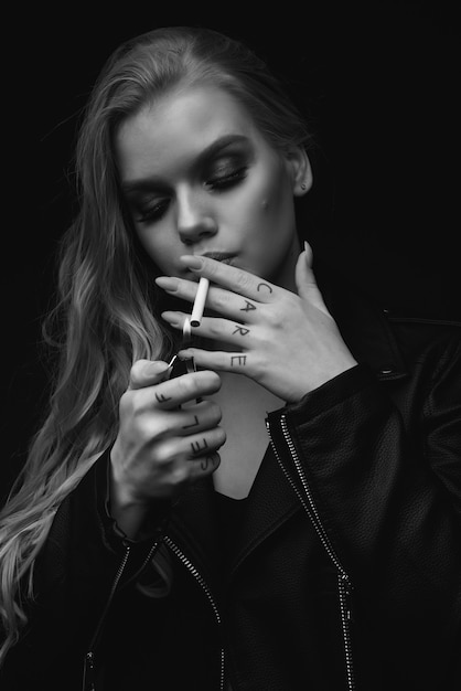 Retrato de hermosa mujer rubia. Chica enciende un cigarrillo, tatuadora. chaqueta.