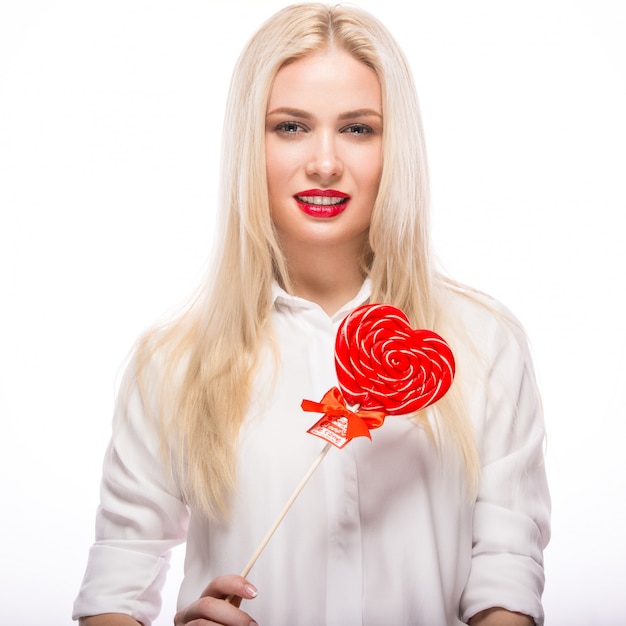 Retrato de hermosa mujer rubia con maquillaje brillante y corazón de caramelo rojo en la mano