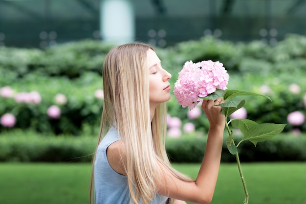 Retrato de hermosa mujer rubia oliendo flores de hortensias en el parque