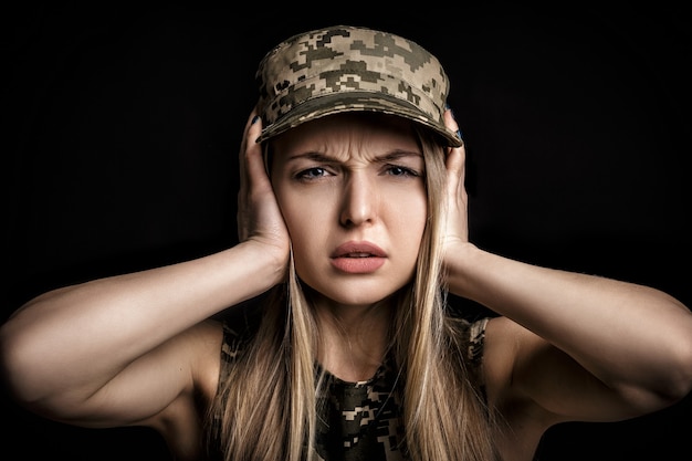 Retrato de una hermosa mujer rubia soldados en traje militar cierra sus oídos con las manos sobre fondo negro