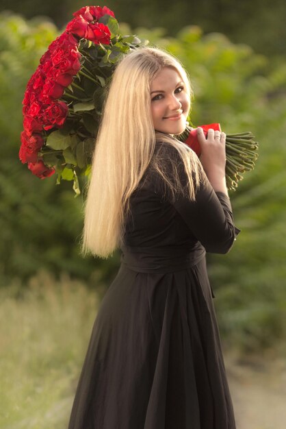 Retrato de una hermosa mujer rubia sosteniendo un gran ramo de cien rosas rojas