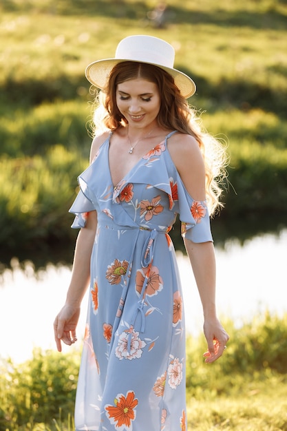 Retrato de una hermosa mujer con sombrero caminando en la hierba verde en el campo cerca del río, la naturaleza en las vacaciones de verano.