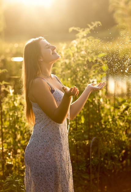 Retrato de hermosa mujer sonriente atrapando gotas de agua en el jardín